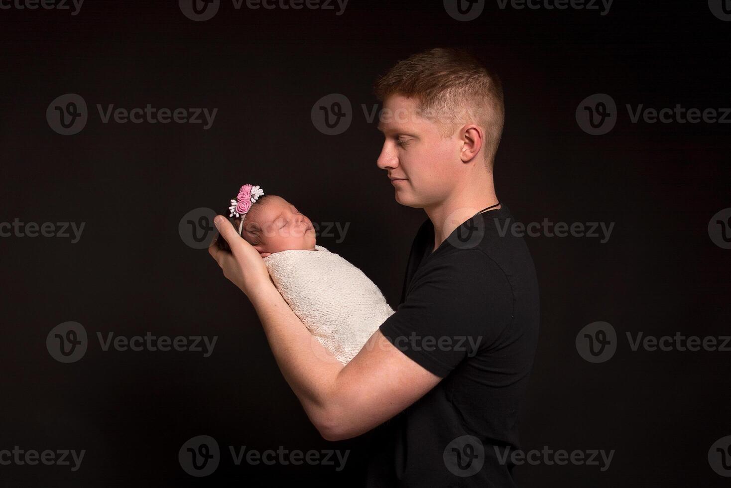 Red-haired father and newborn daughter on a black background. photo