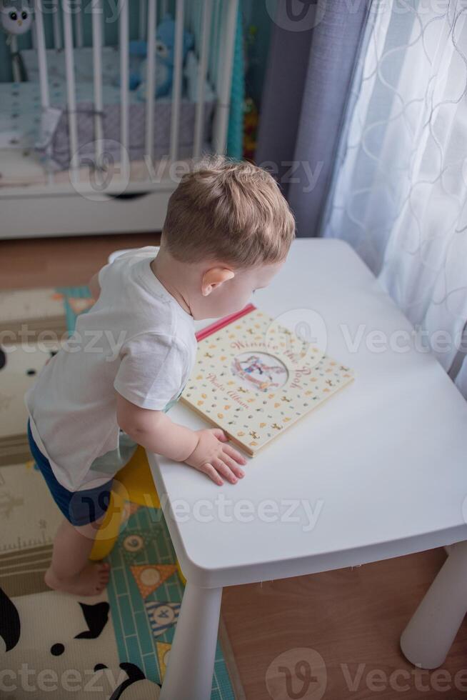 A boy, a child sits at a white table and reads a book. photo