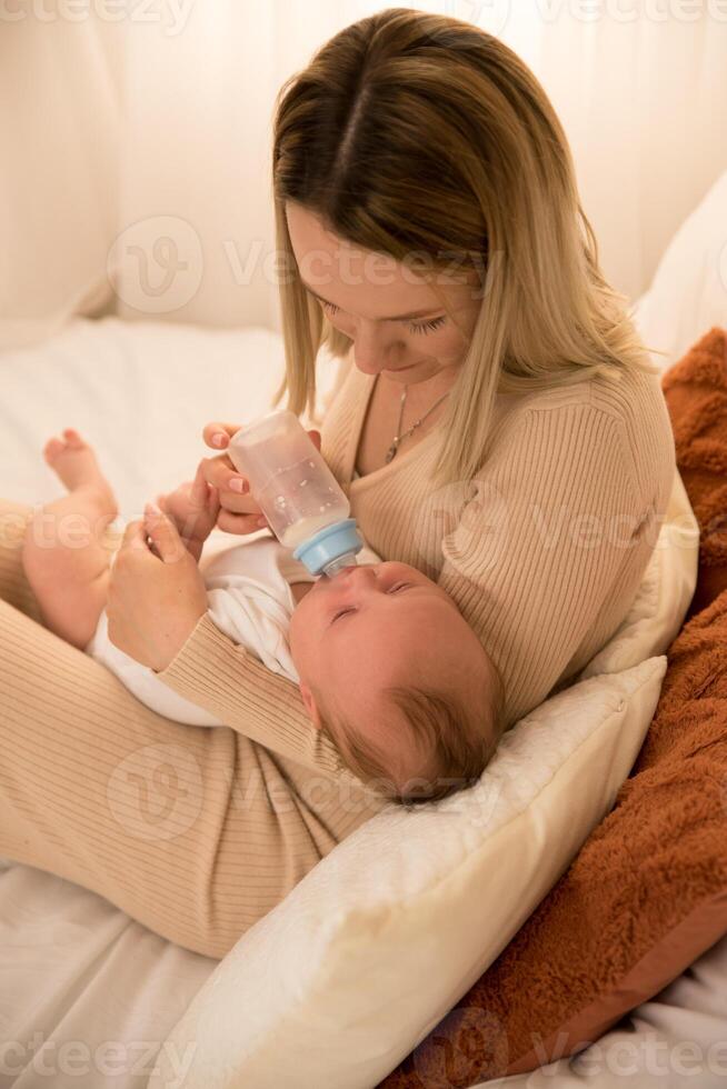 mom feeds a newborn baby with a bottle. the sun is shining in the background. photo