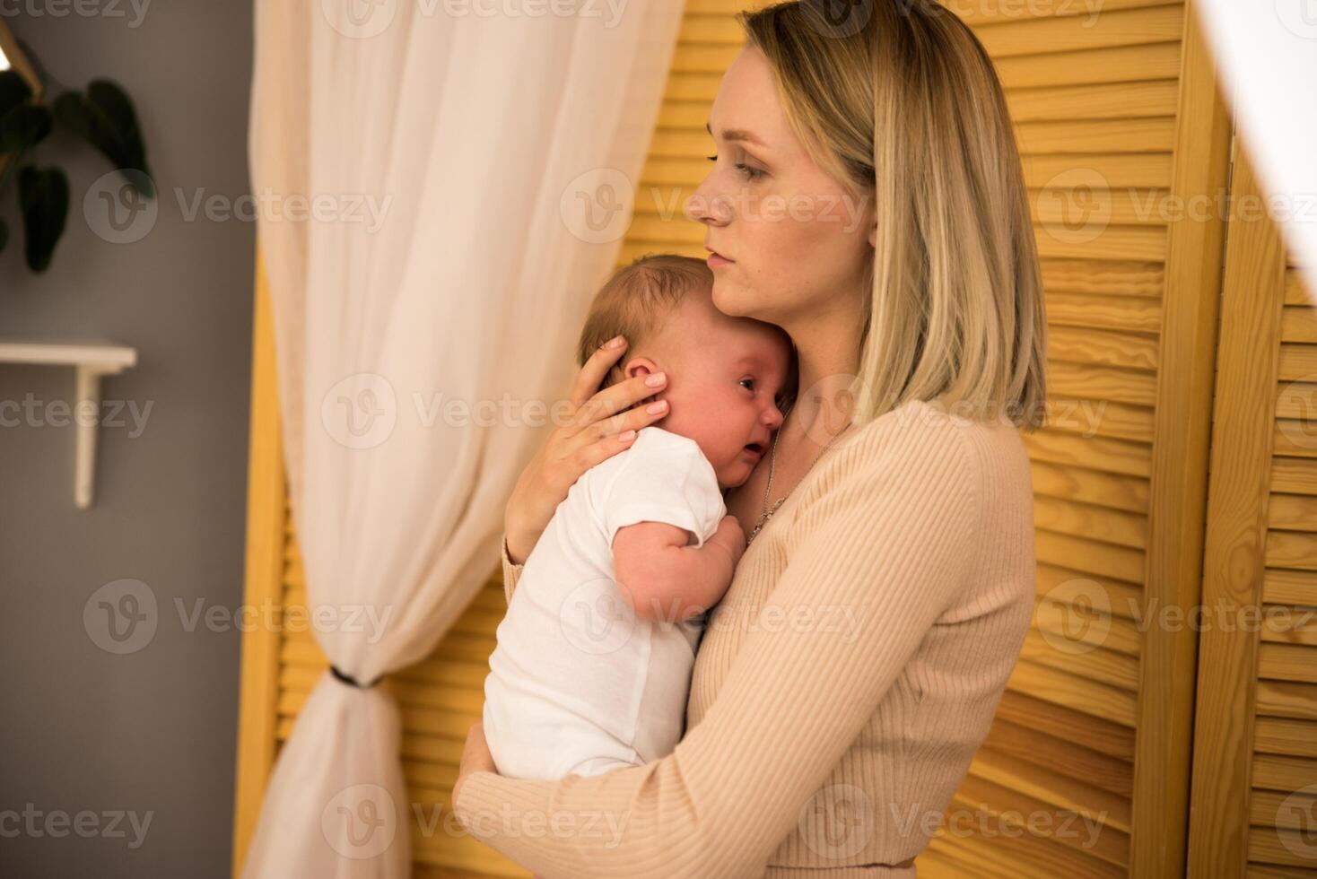 mom holds a newborn baby in her arms. in the background the sun shines from the window. photo