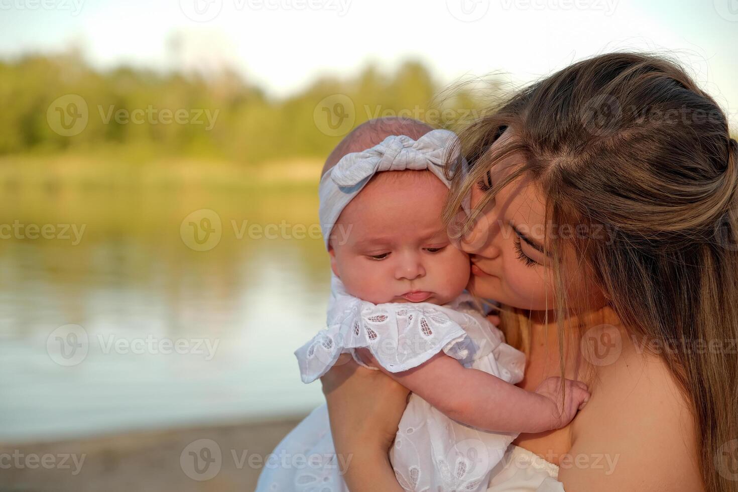 a beautiful girl in a white dress with a newborn baby is sitting on the beach, on the sand. photo