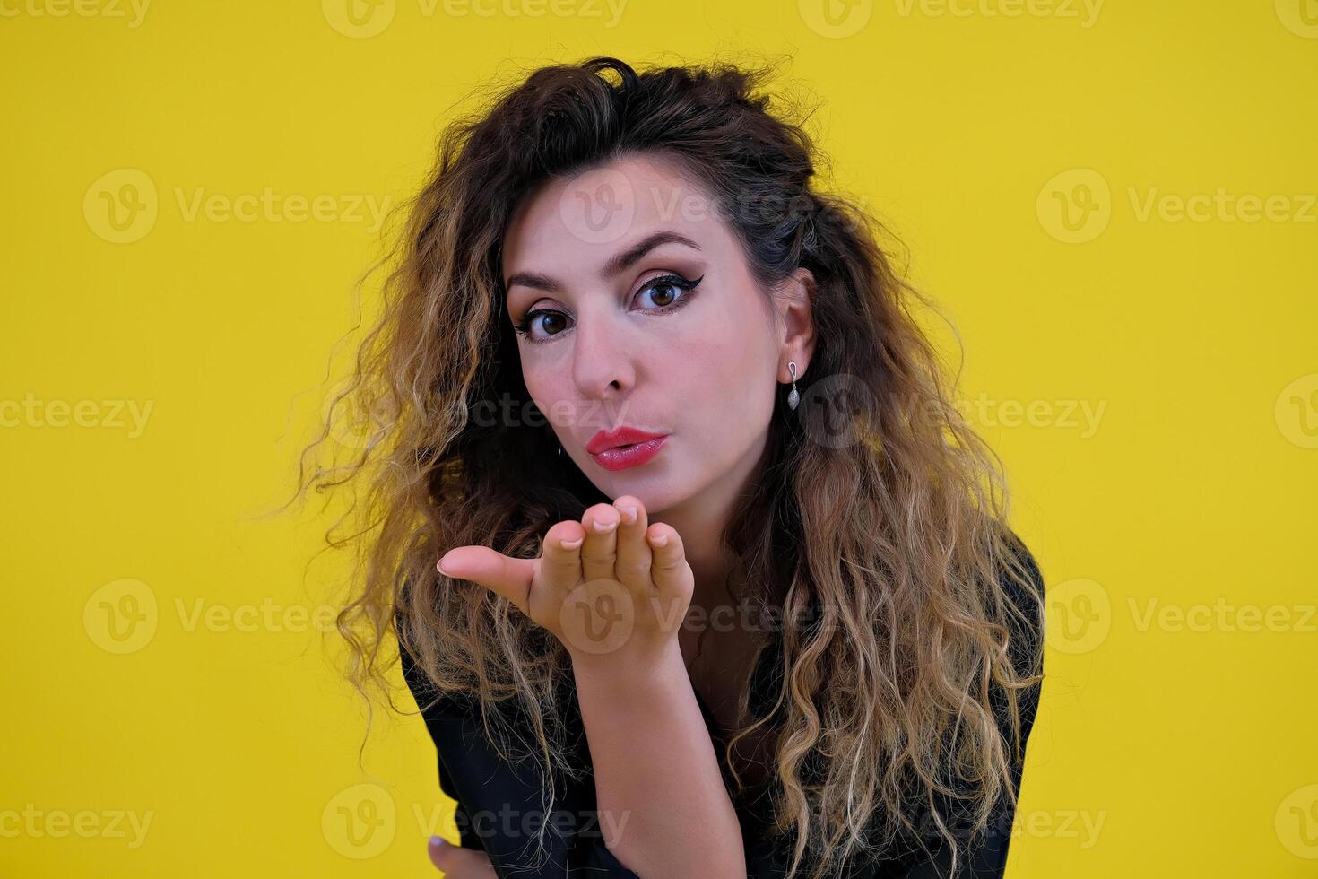 Close-up portrait of a beautiful girl on a yellow background. a woman makes an air kiss. positive human emotions photo