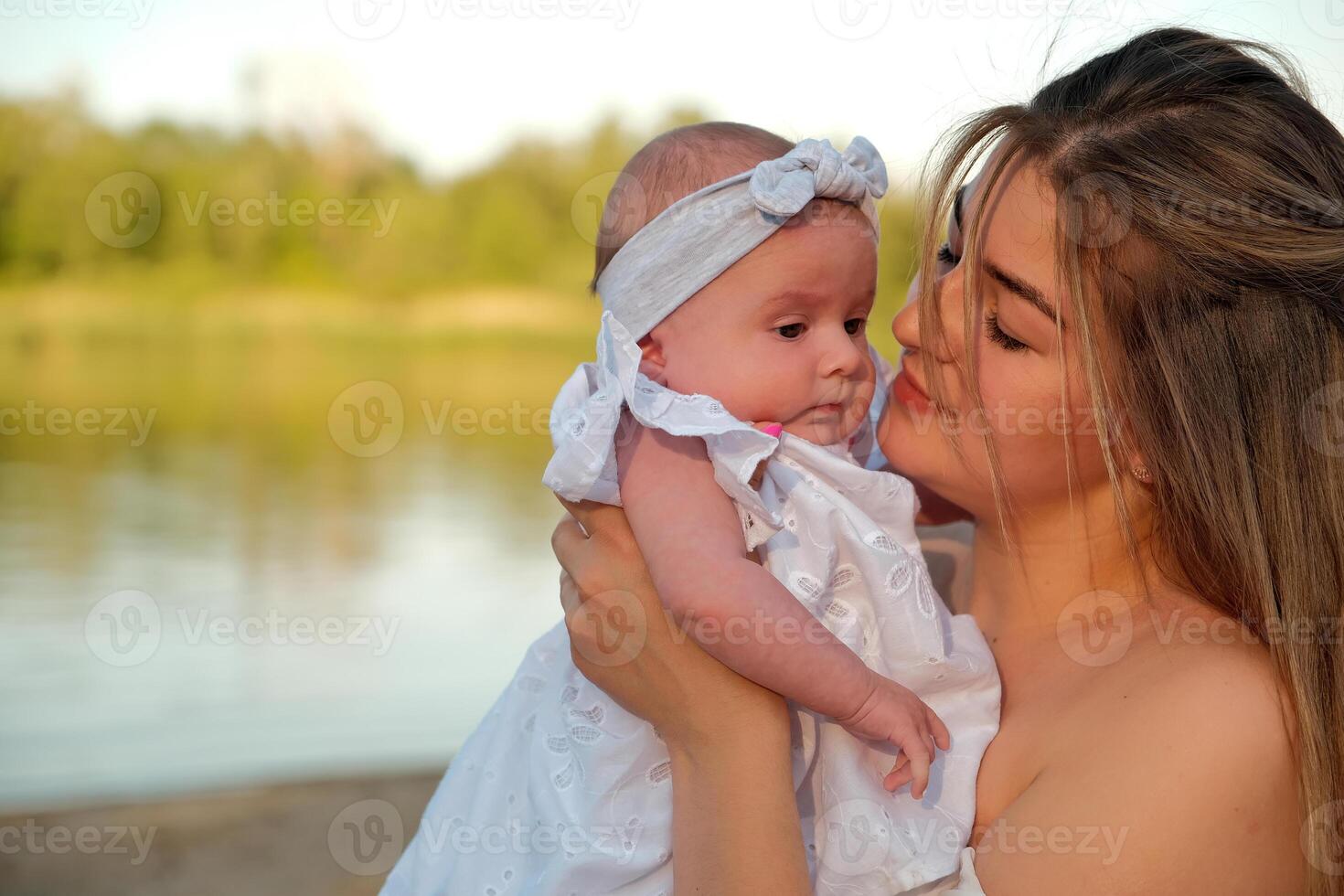 a beautiful girl in a white dress with a newborn baby is sitting on the beach, on the sand. photo