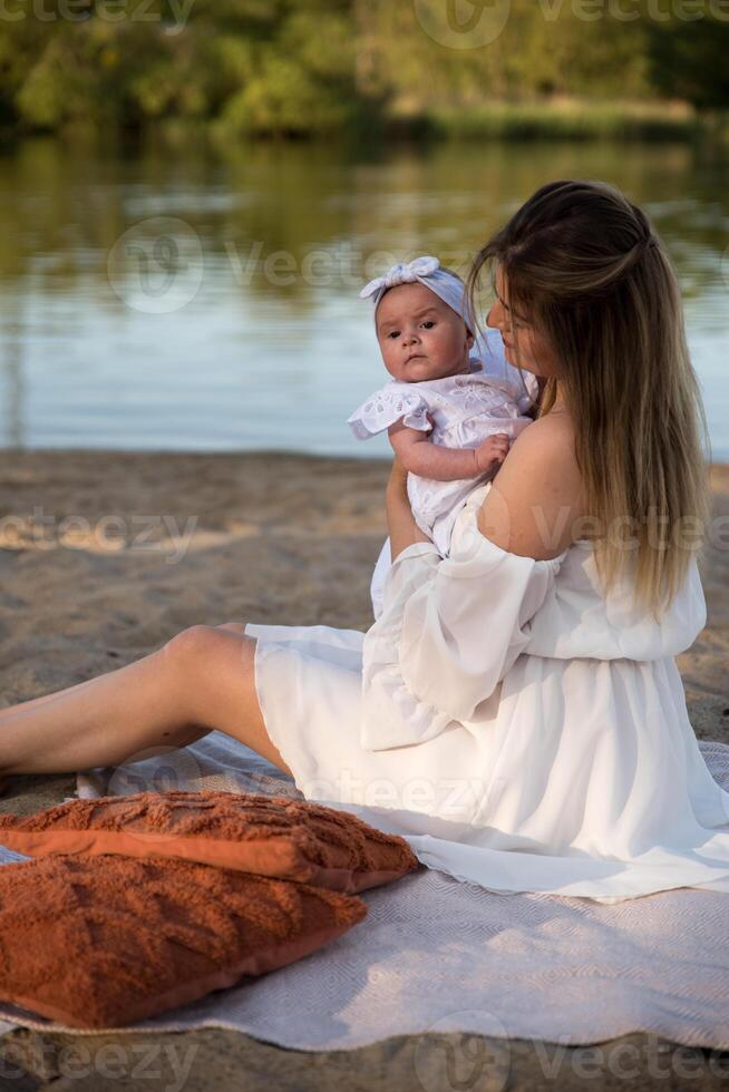 mom with a newborn baby sits on the beach, on the sand. mom holds a newborn baby in her arms. photo