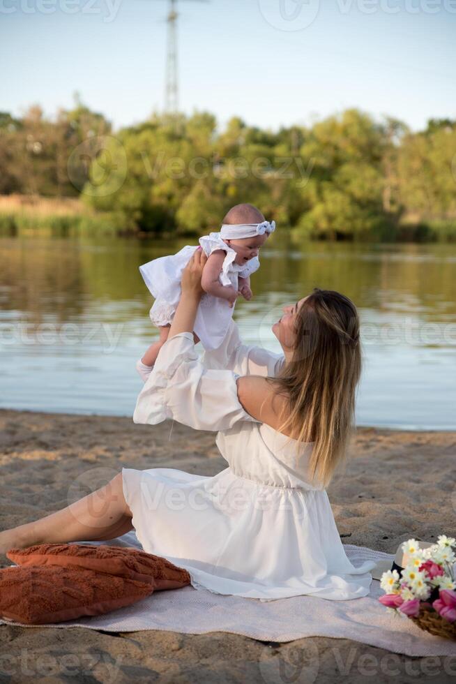 mom with a newborn baby sits on the beach, on the sand. mom holds a newborn baby in her arms. photo