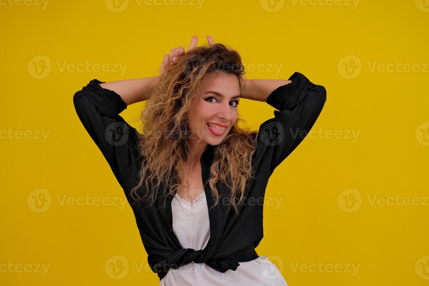 beautiful girl on a yellow background. Pretty brave woman showing wild devilish side making bull horns with her fingers on her head. photo