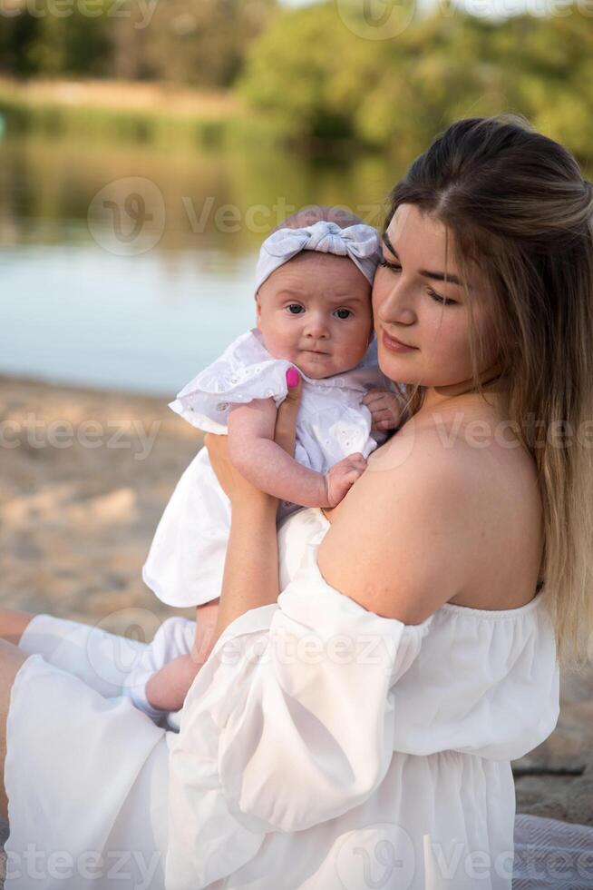 mom with a newborn baby sits on the beach, on the sand. mom holds a newborn baby in her arms. photo