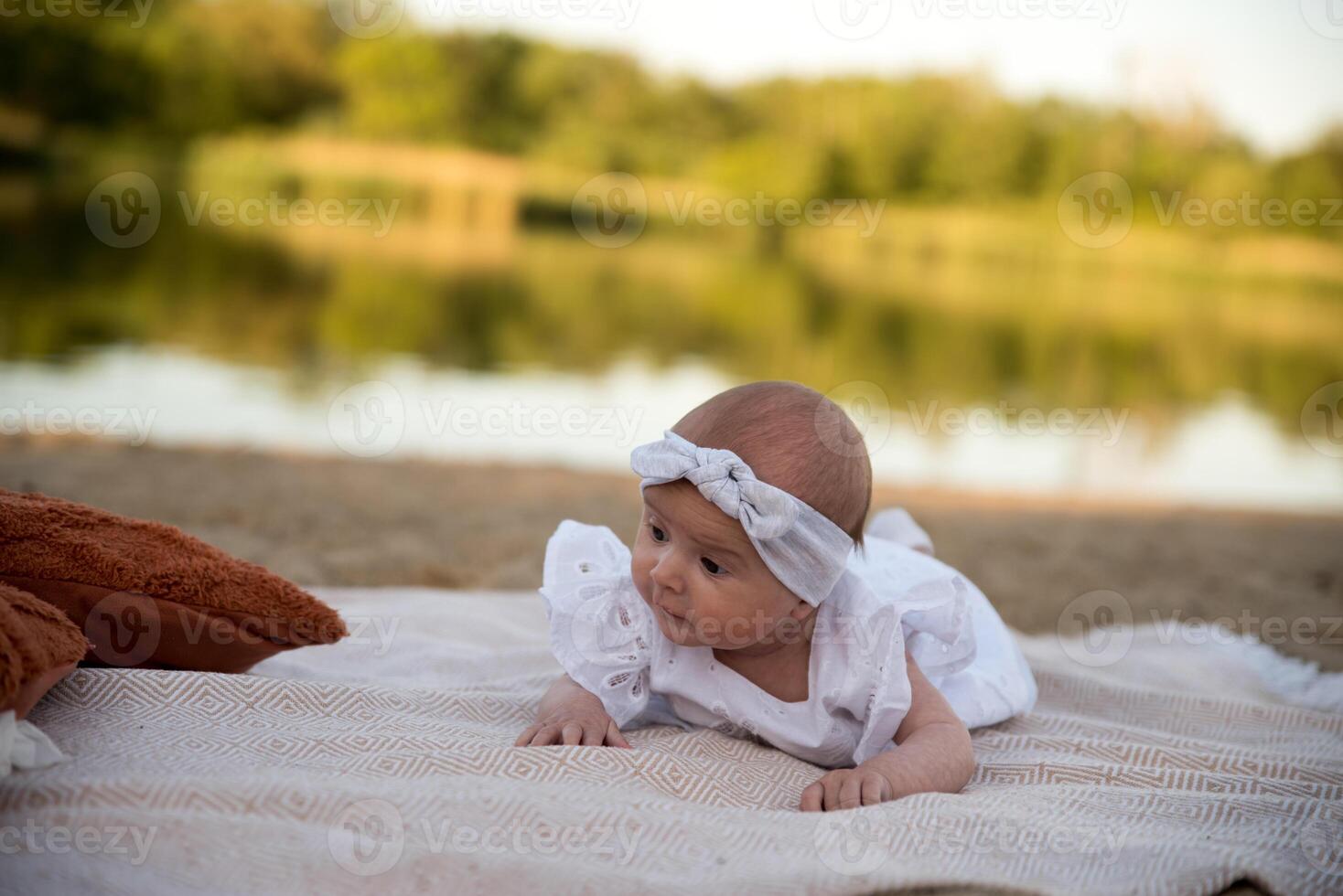 a newborn child lies on a blanket, on the shore. flowers lie nearby. photo