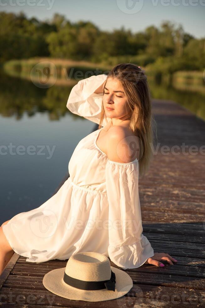 a beautiful girl in a hat stands on the shore. hat in hand. photo