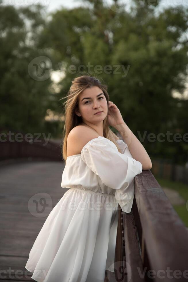 a beautiful girl in a white dress stands on a wooden bridge. photo