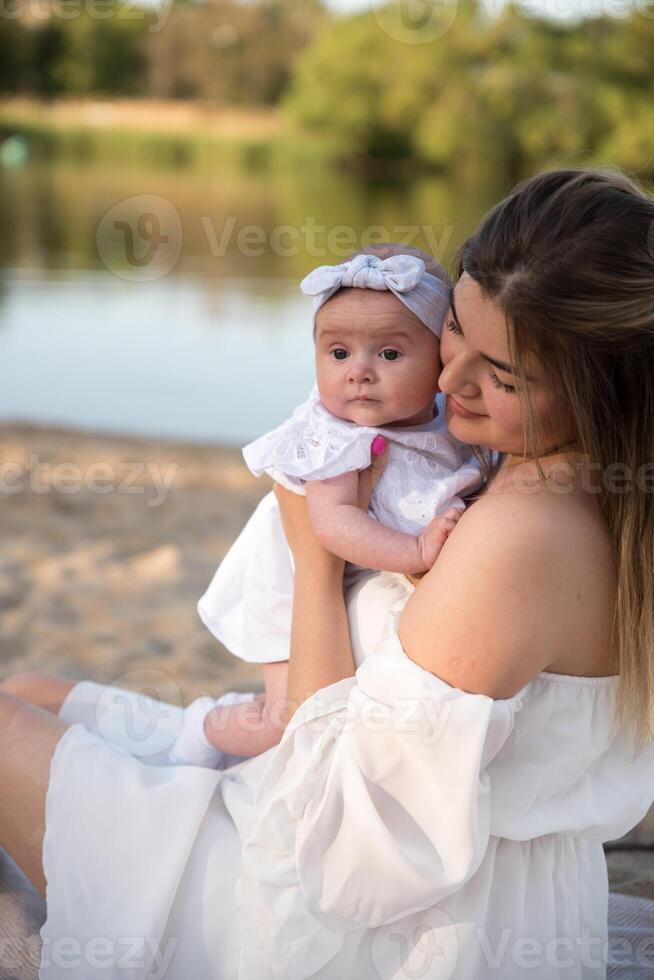 mom with a newborn baby sits on the beach, on the sand. mom holds a newborn baby in her arms. photo