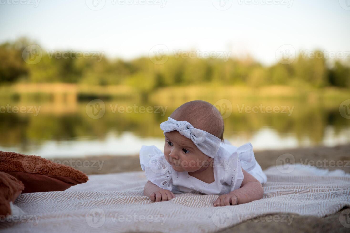 a newborn child lies on a blanket, on the shore. flowers lie nearby. photo