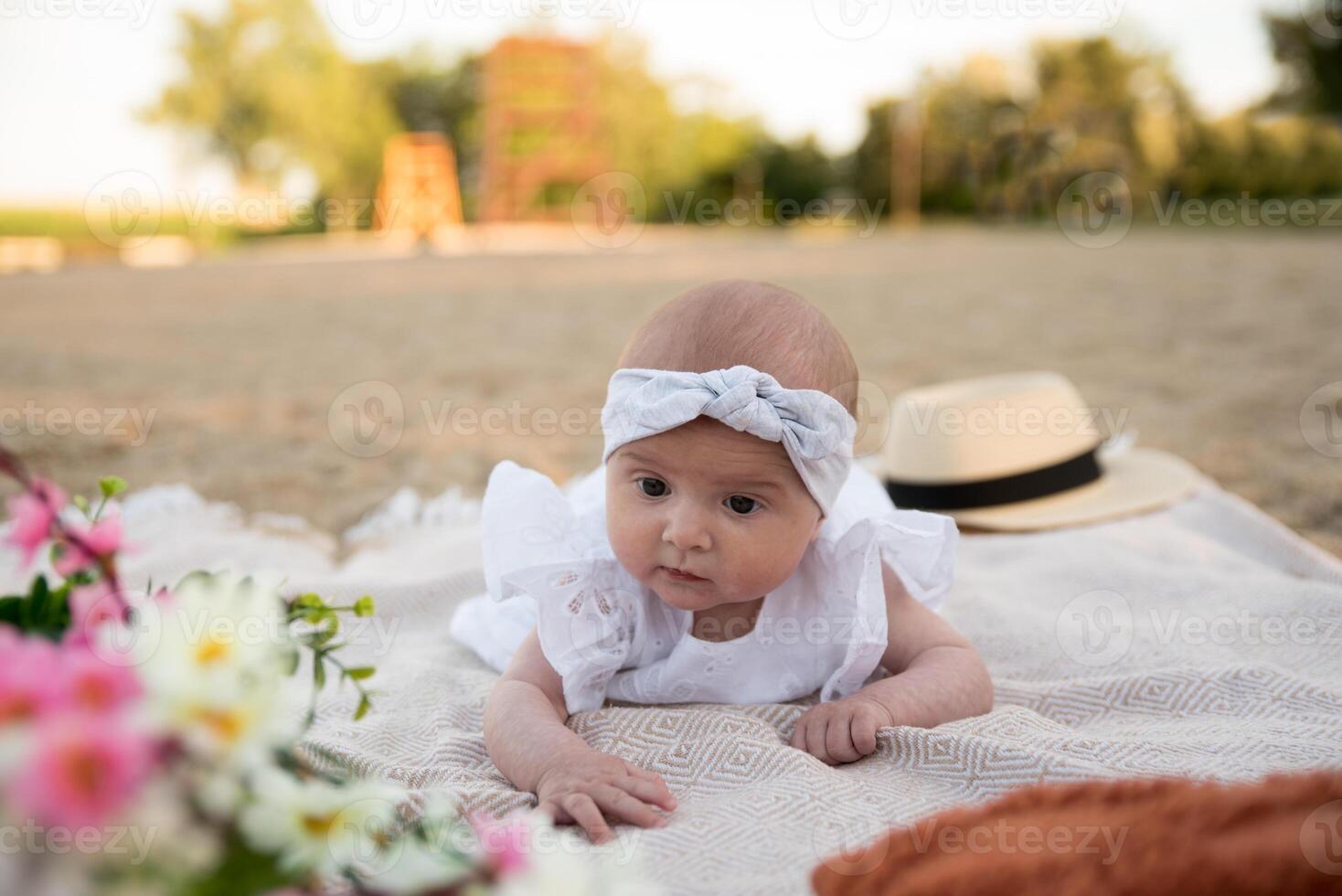 a newborn child lies on a blanket, on the shore. flowers lie nearby. photo