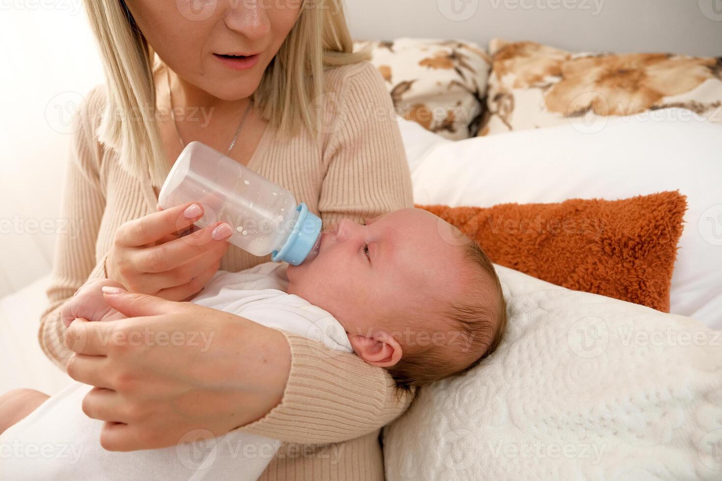 mom feeds a newborn baby with a bottle. the sun is shining in the background. photo