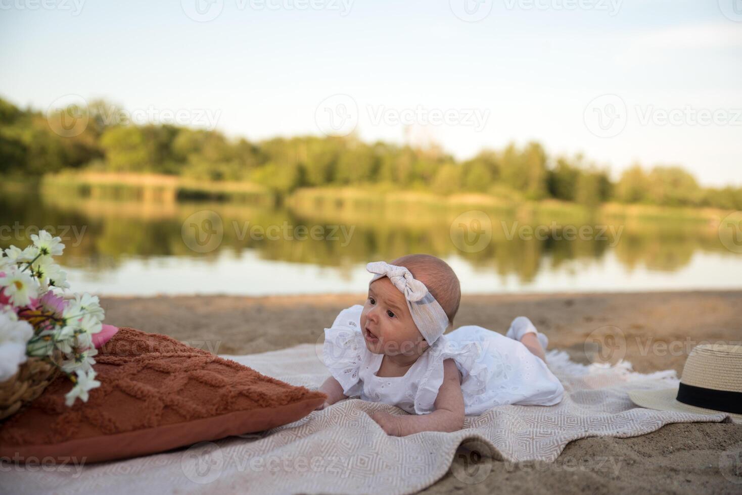 a newborn child lies on a blanket, on the shore. flowers lie nearby. photo