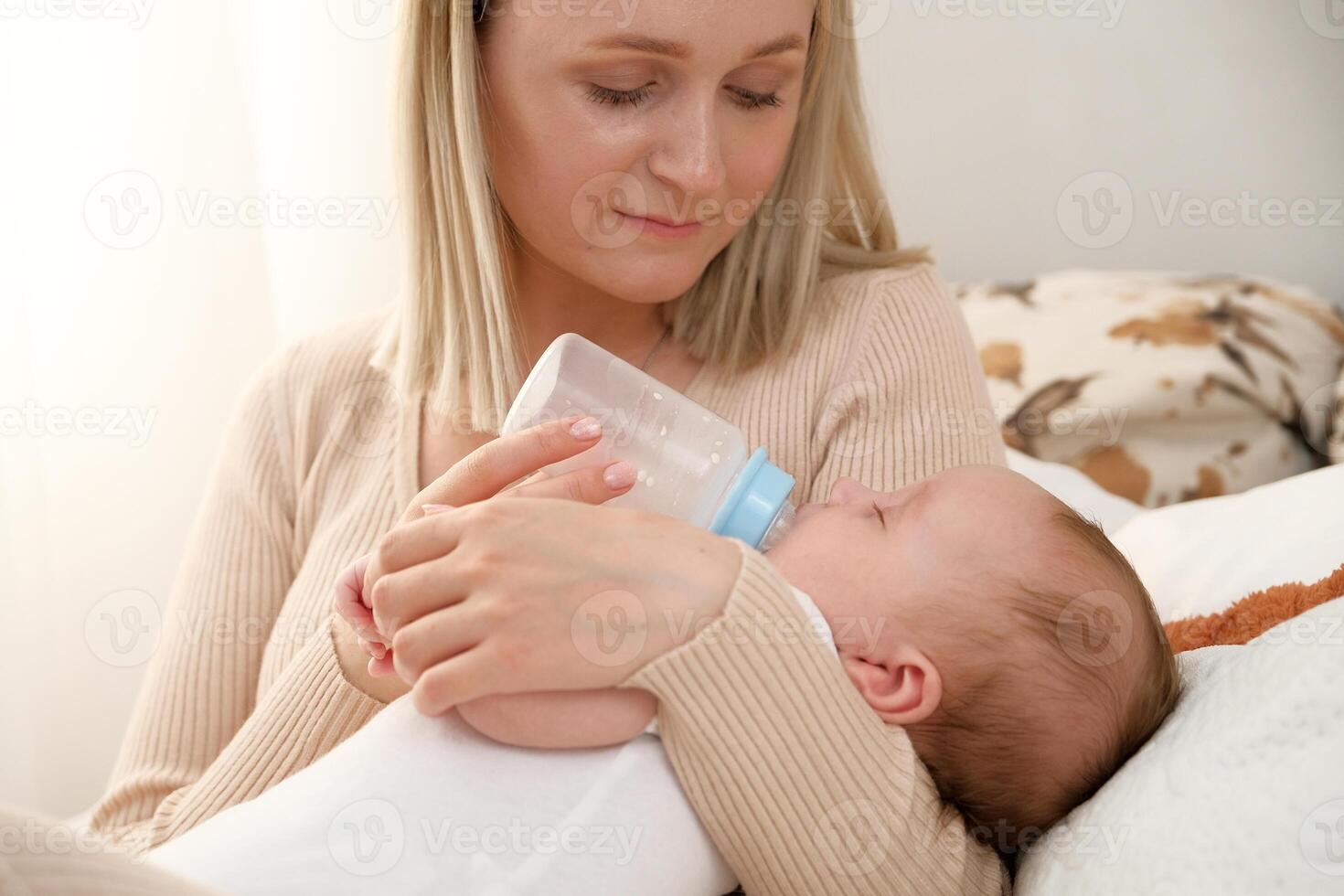 mom feeds a newborn baby with a bottle. the sun is shining in the background. photo