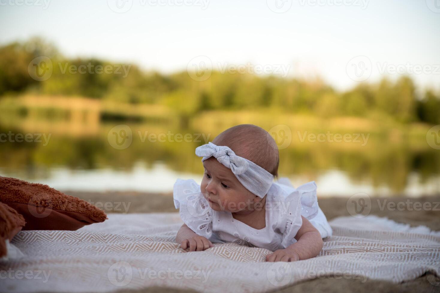 a newborn child lies on a blanket, on the shore. flowers lie nearby. photo