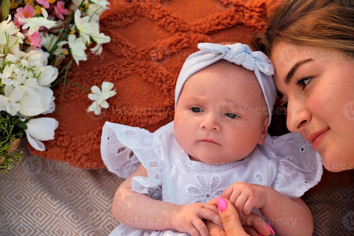 mom with a newborn baby lie on the beach. white dresses. flowers lie nearby. photo
