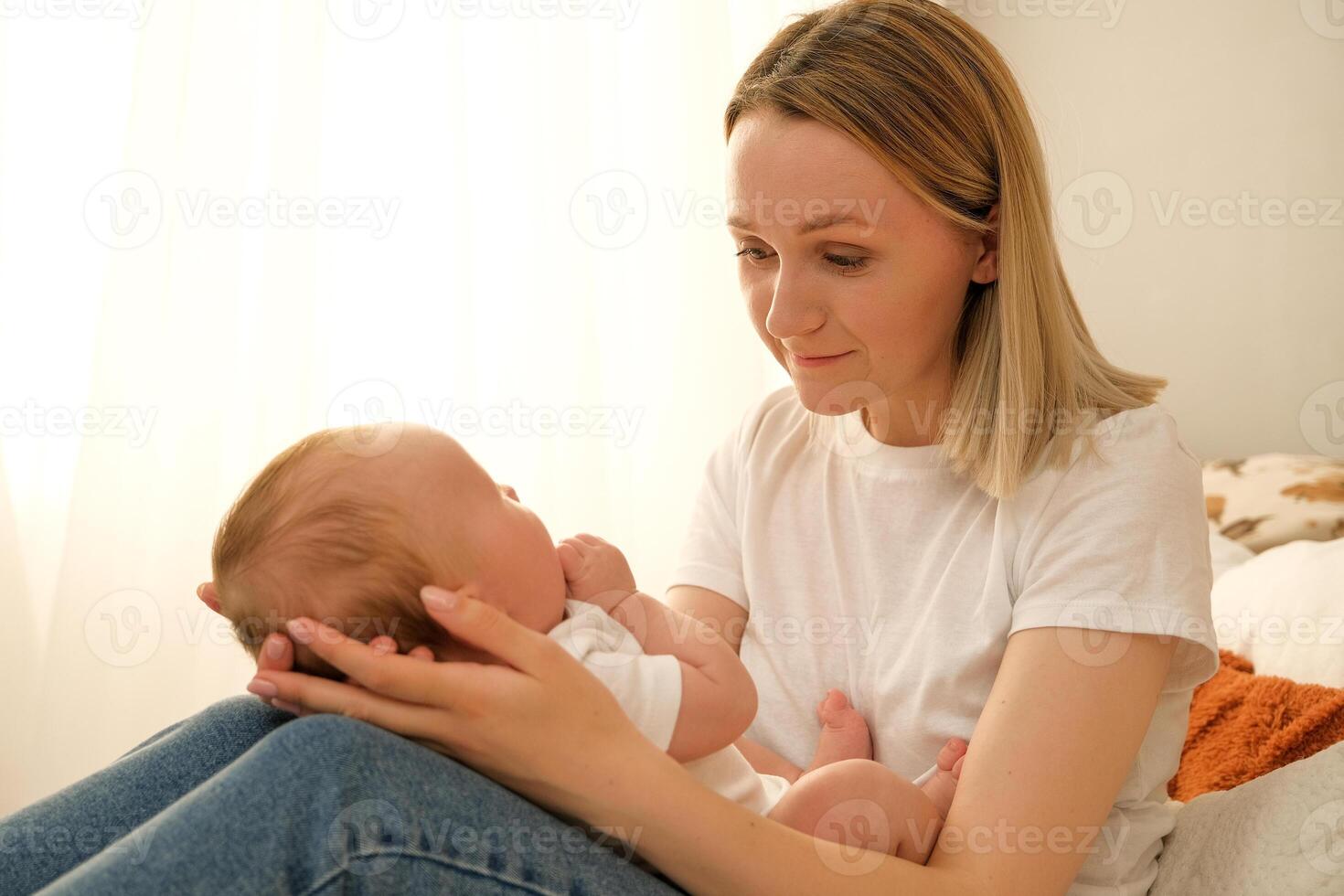 mom holds a newborn baby in her arms. in the background the sun shines from the window. photo