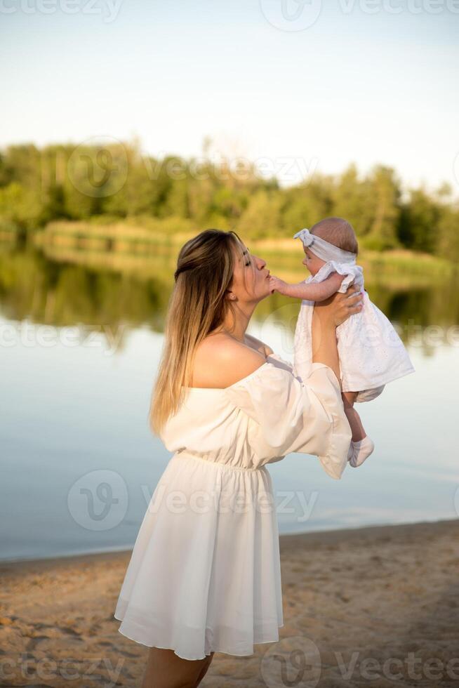 mom with a newborn baby sits on the beach, on the sand. mom holds a newborn baby in her arms. photo
