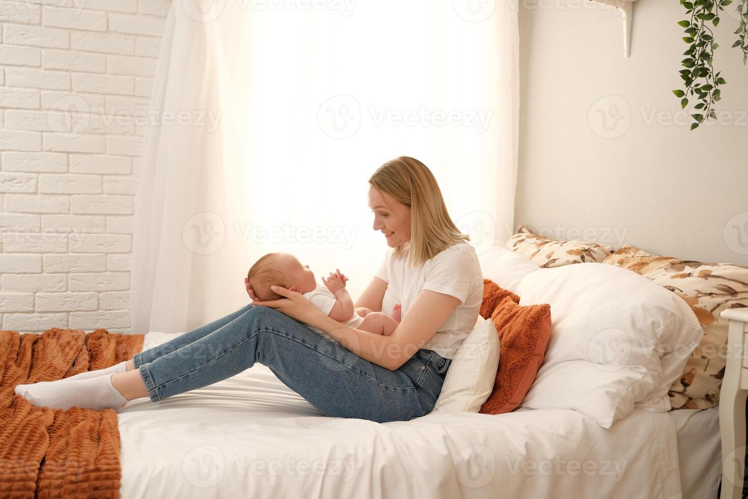 mom holds a newborn baby in her arms. in the background the sun shines from the window. photo