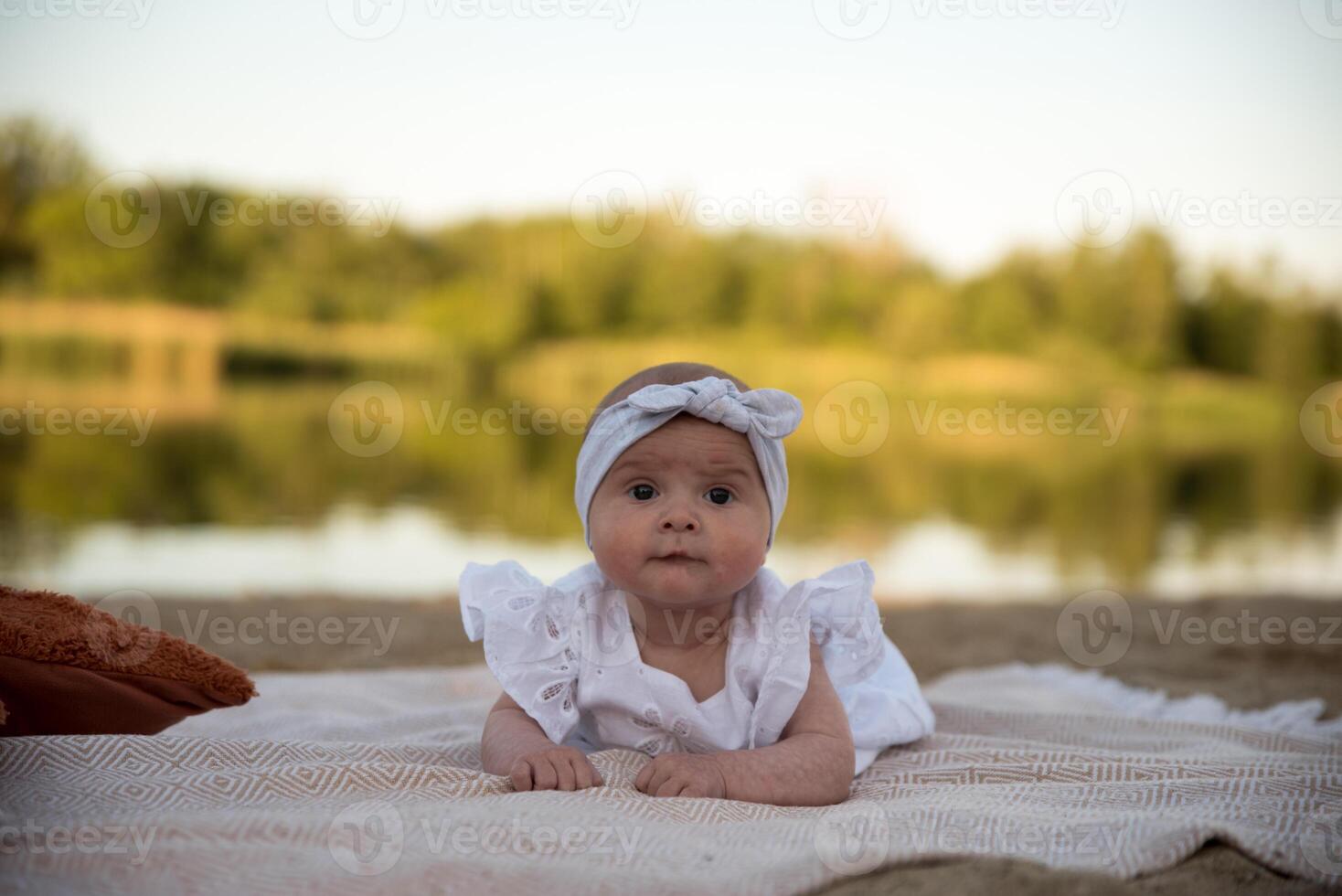 a newborn child lies on a blanket, on the shore. flowers lie nearby. photo