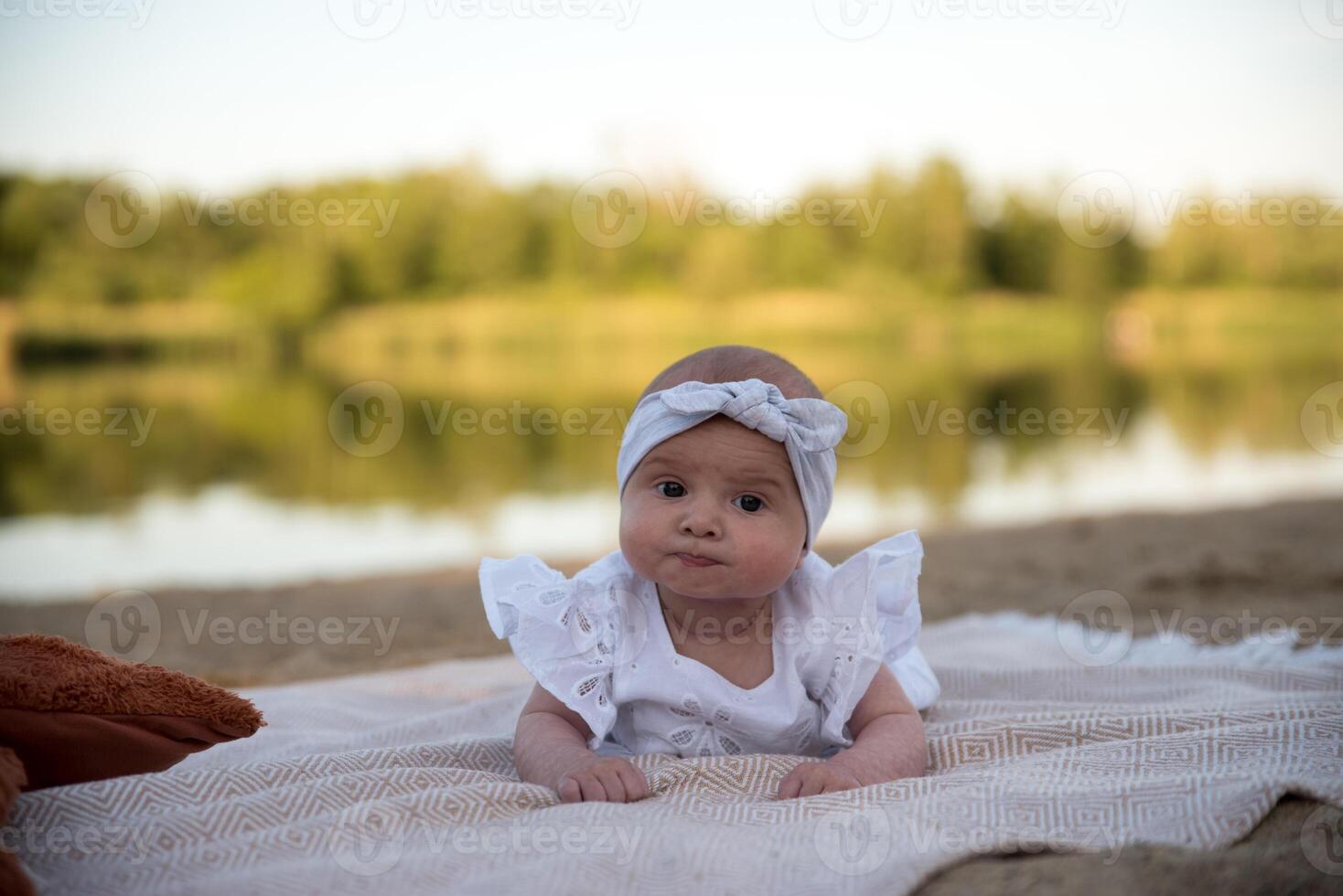 a newborn child lies on a blanket, on the shore. flowers lie nearby. photo