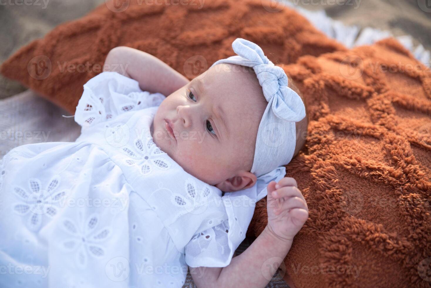 a newborn child lies on a blanket, on the shore. flowers lie nearby. photo