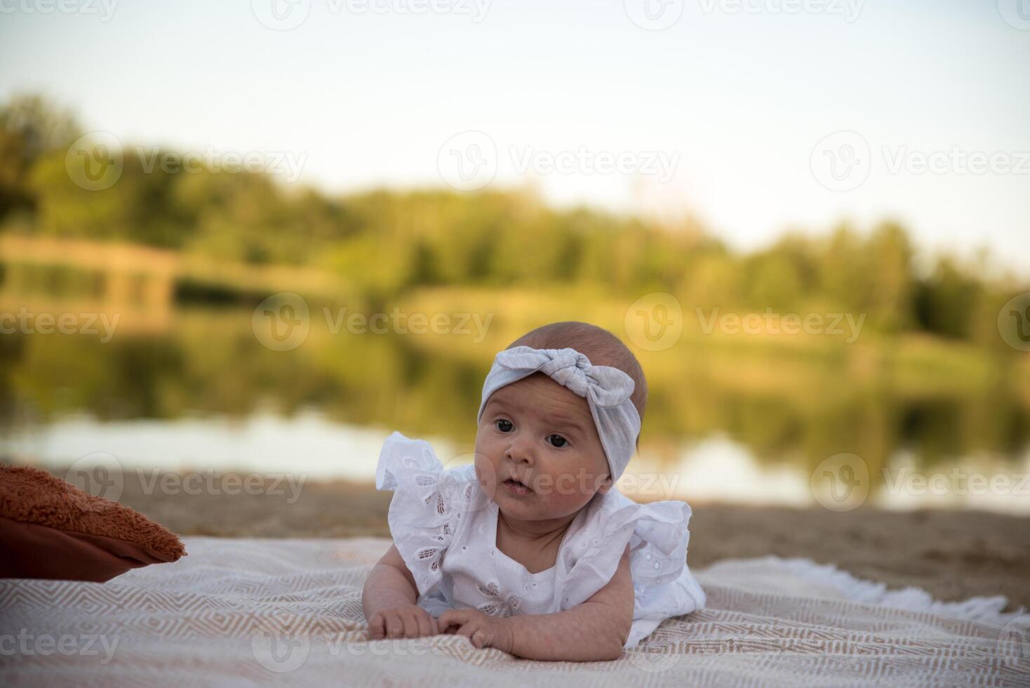 a newborn child lies on a blanket, on the shore. flowers lie nearby. photo