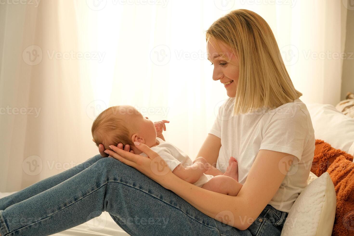 mom holds a newborn baby in her arms. in the background the sun shines from the window. photo