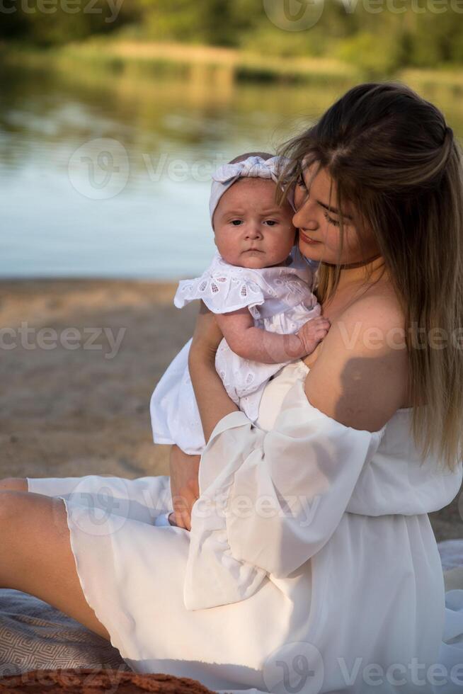 mom with a newborn baby sits on the beach, on the sand. mom holds a newborn baby in her arms. photo