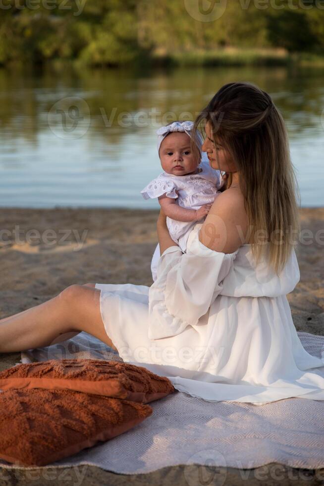 mom with a newborn baby sits on the beach, on the sand. mom holds a newborn baby in her arms. photo