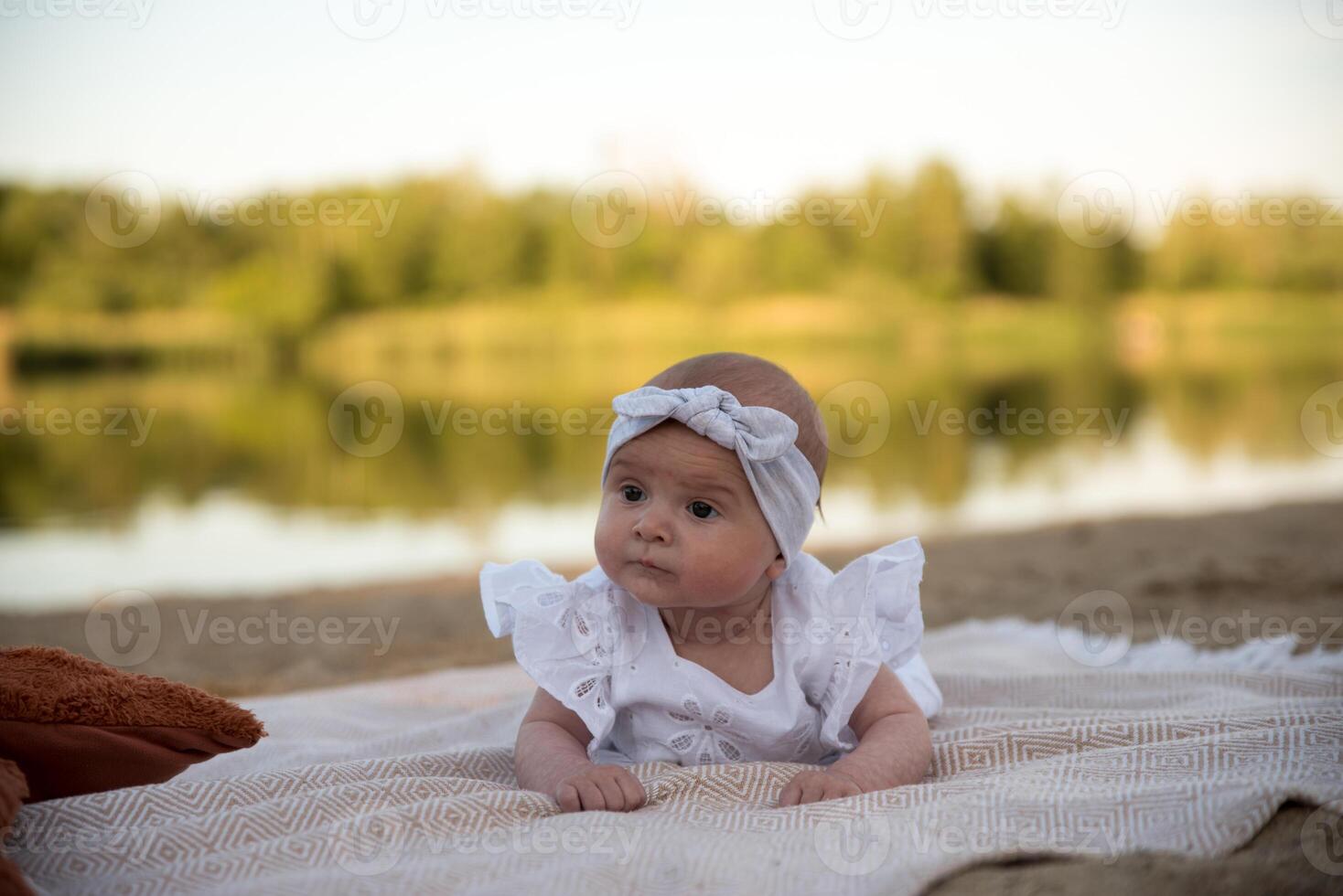 a newborn child lies on a blanket, on the shore. flowers lie nearby. photo