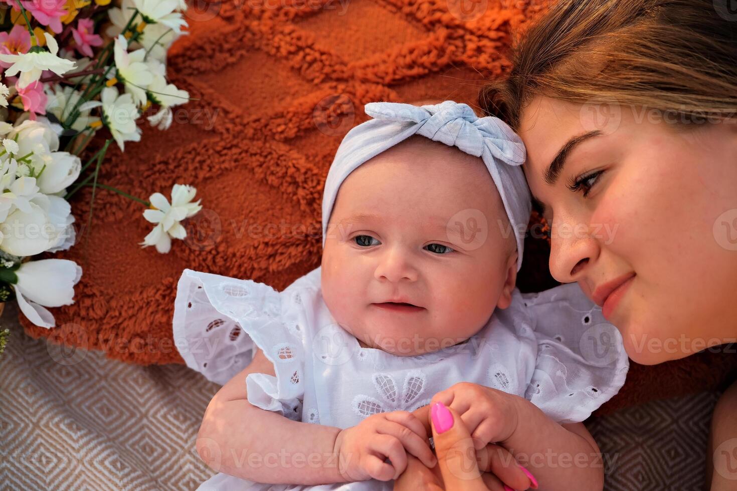 mom with a newborn baby lie on the beach. white dresses. flowers lie nearby. photo