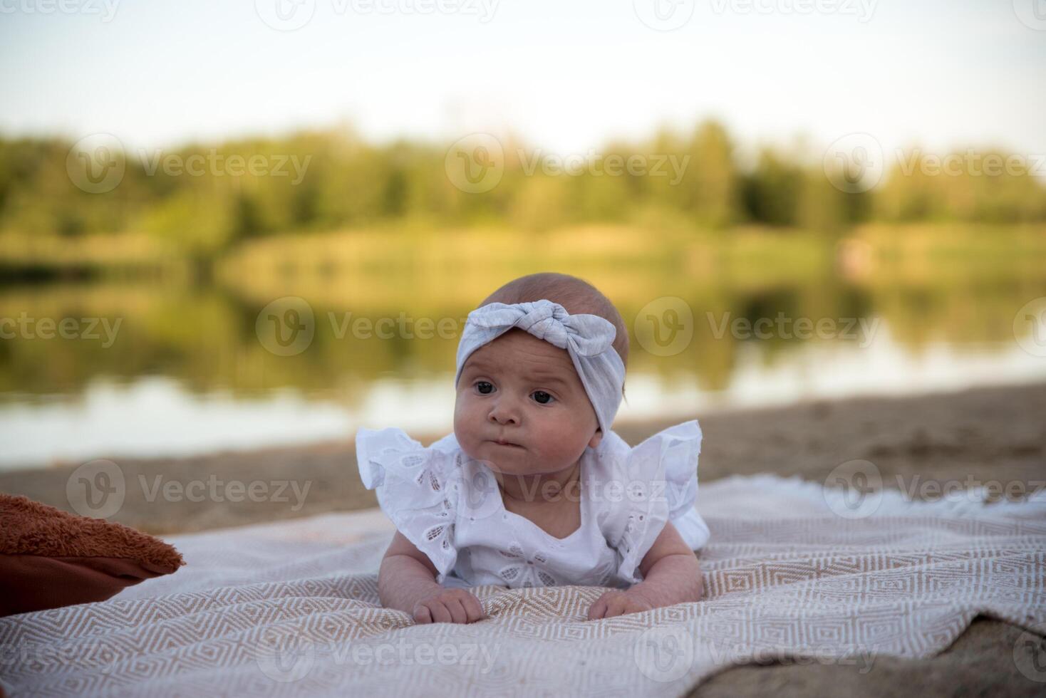a newborn child lies on a blanket, on the shore. flowers lie nearby. photo