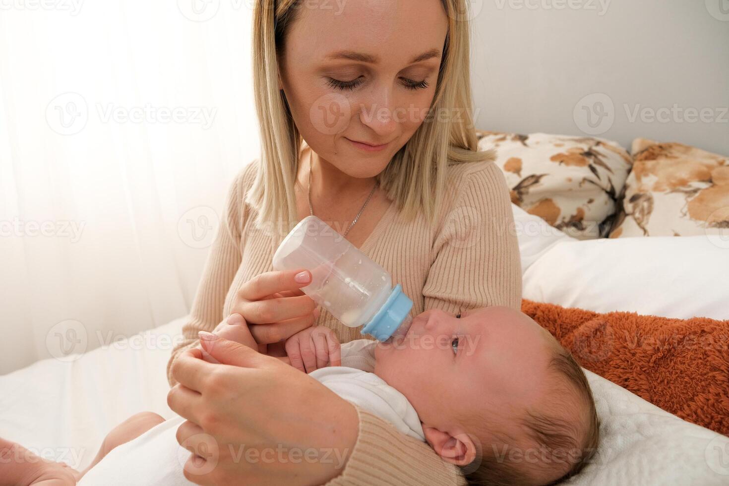 mom feeds a newborn baby with a bottle. the sun is shining in the background. photo