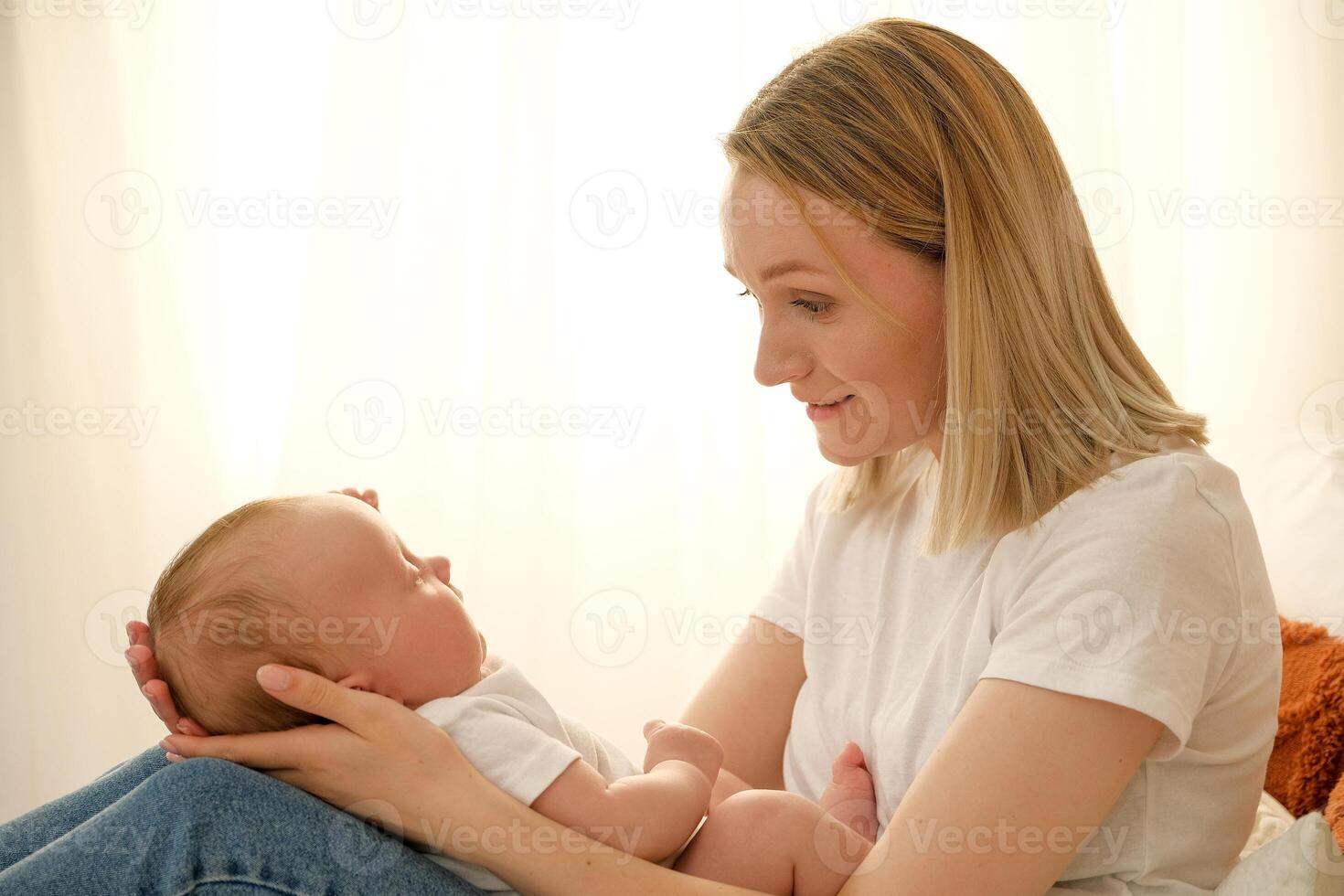 mom holds a newborn baby in her arms. in the background the sun shines from the window. photo
