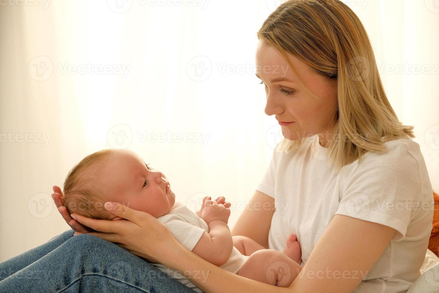 mom holds a newborn baby in her arms. in the background the sun shines from the window. photo