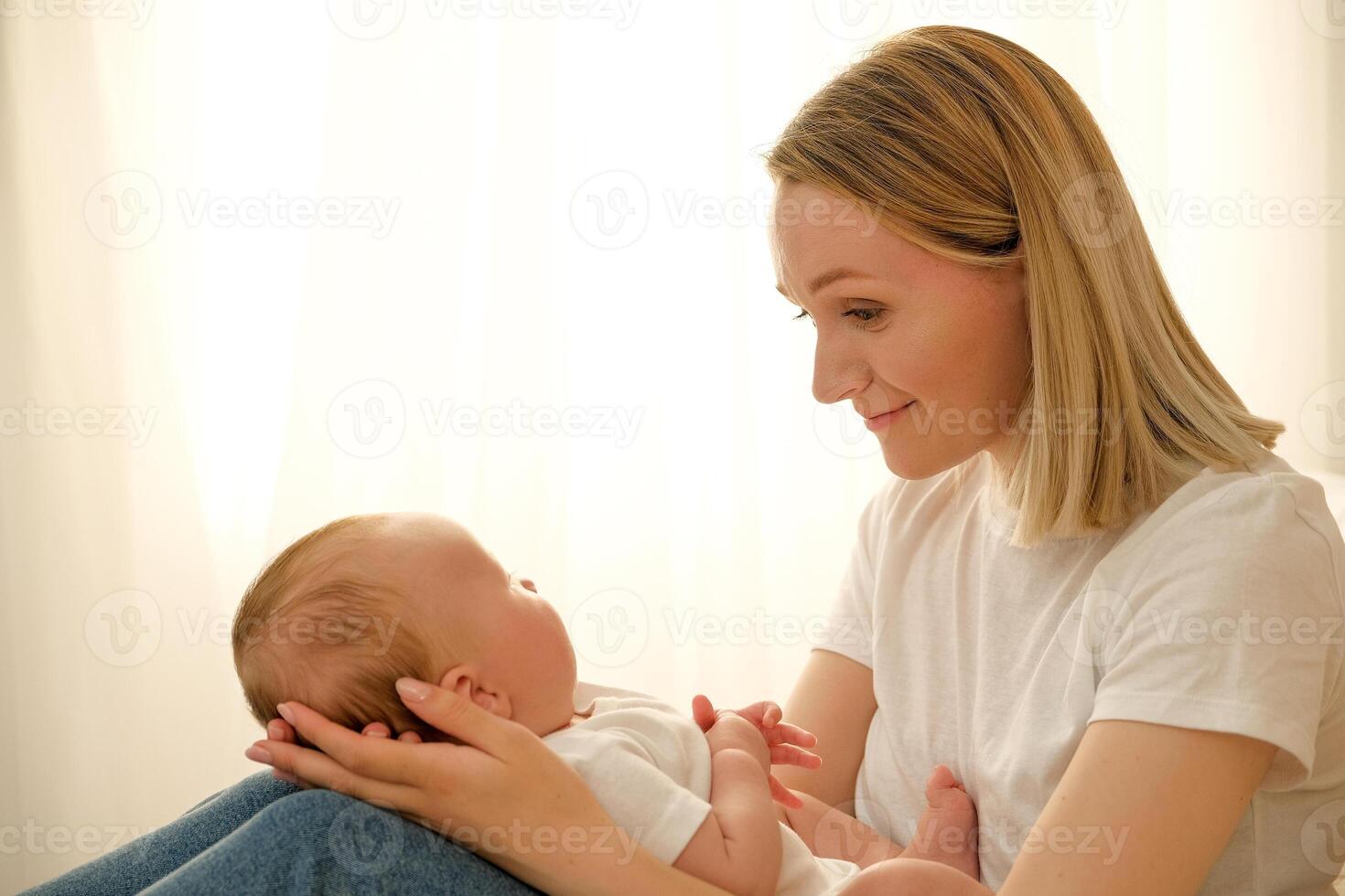 mom holds a newborn baby in her arms. in the background the sun shines from the window. photo