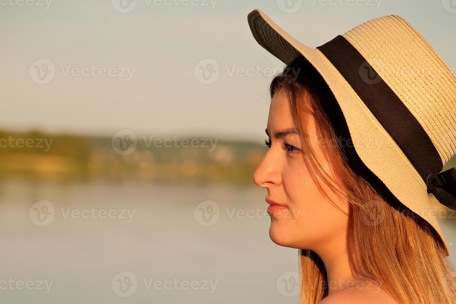 a beautiful girl in a hat stands on the shore. hat in hand. photo