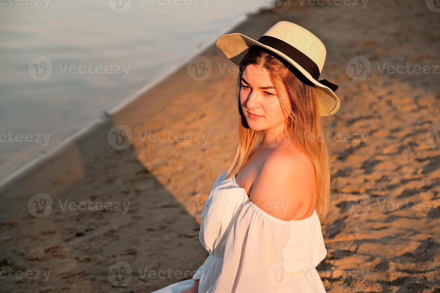 a beautiful girl in a hat stands on the shore. hat in hand. photo
