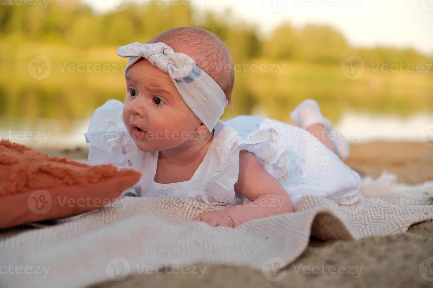 newborn baby girl lies on the beach. in a white dress. photo
