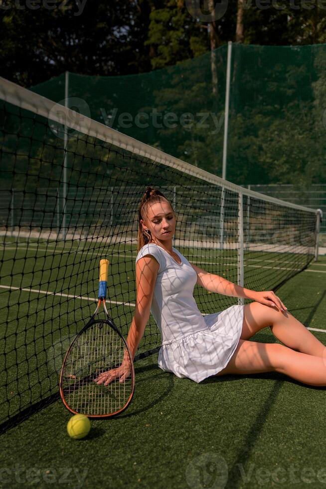 a girl in a white sports dress stands on a tennis court and holds a racket. portrait of a girl on the tennis court. photo