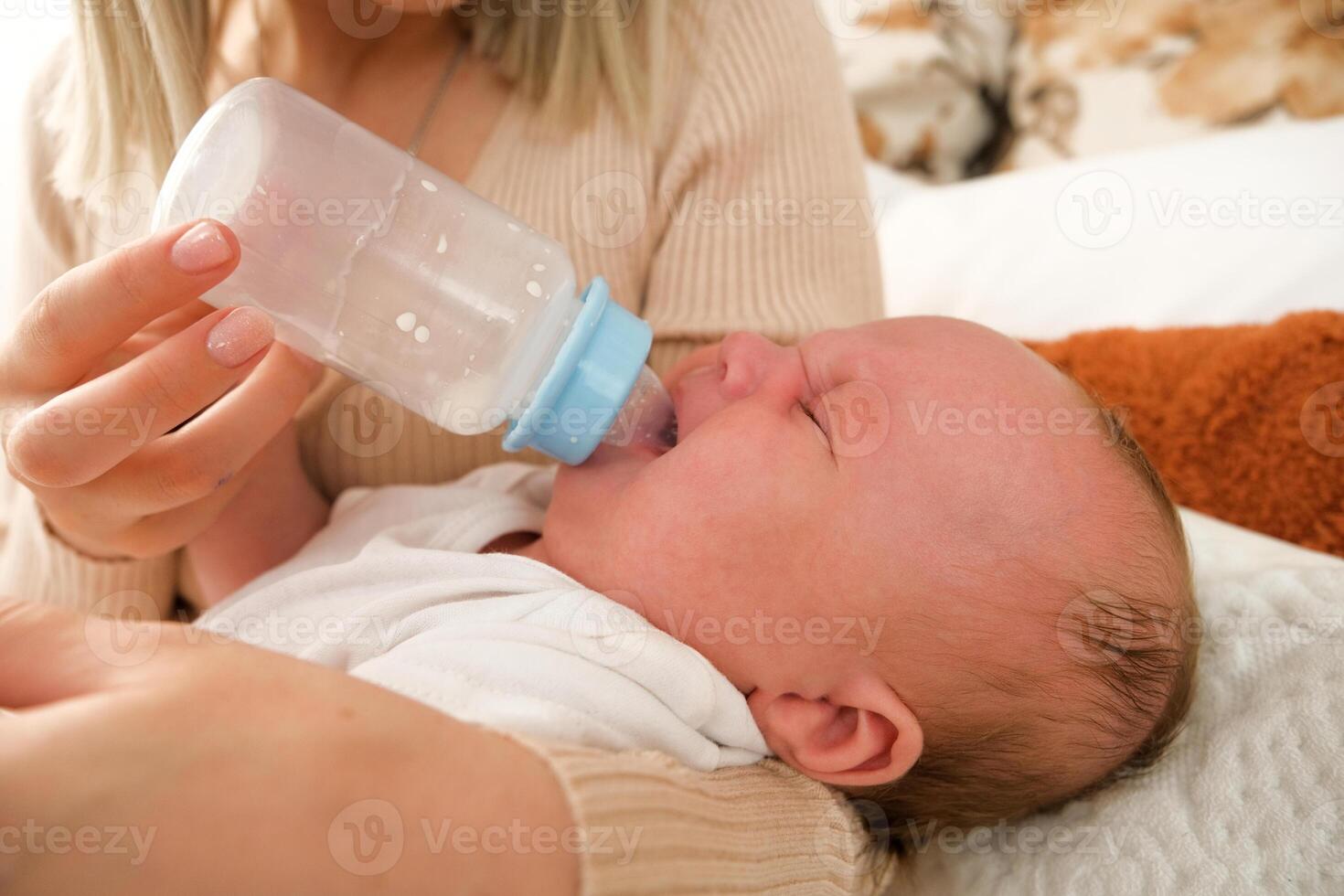 mom feeds a newborn baby with a bottle. the sun is shining in the background. photo