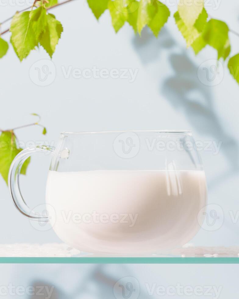 Glass cup of natural milk on a glass shelf with green branch photo