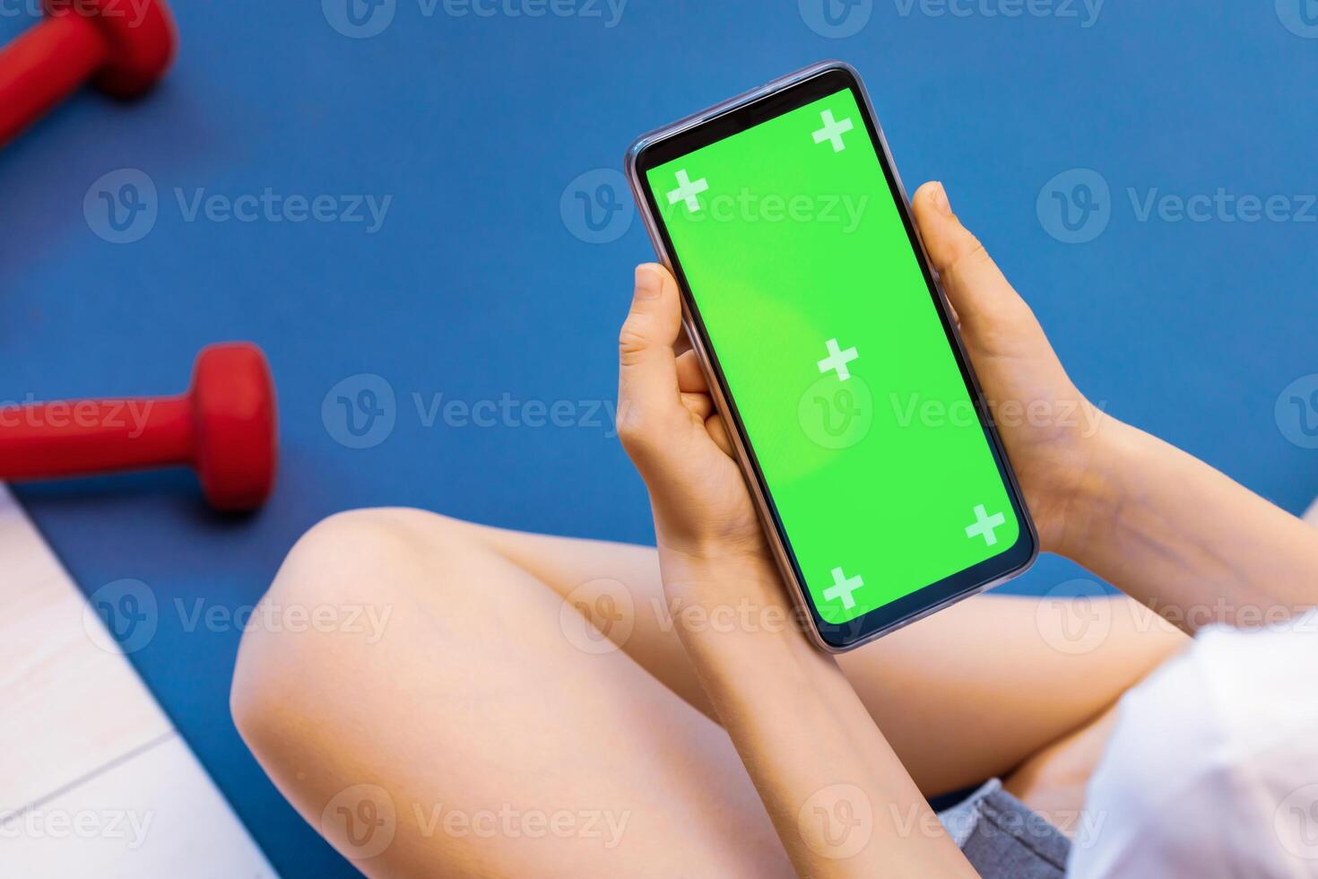 Boy sitting on a gym mat and holding the smartphone with green screen photo