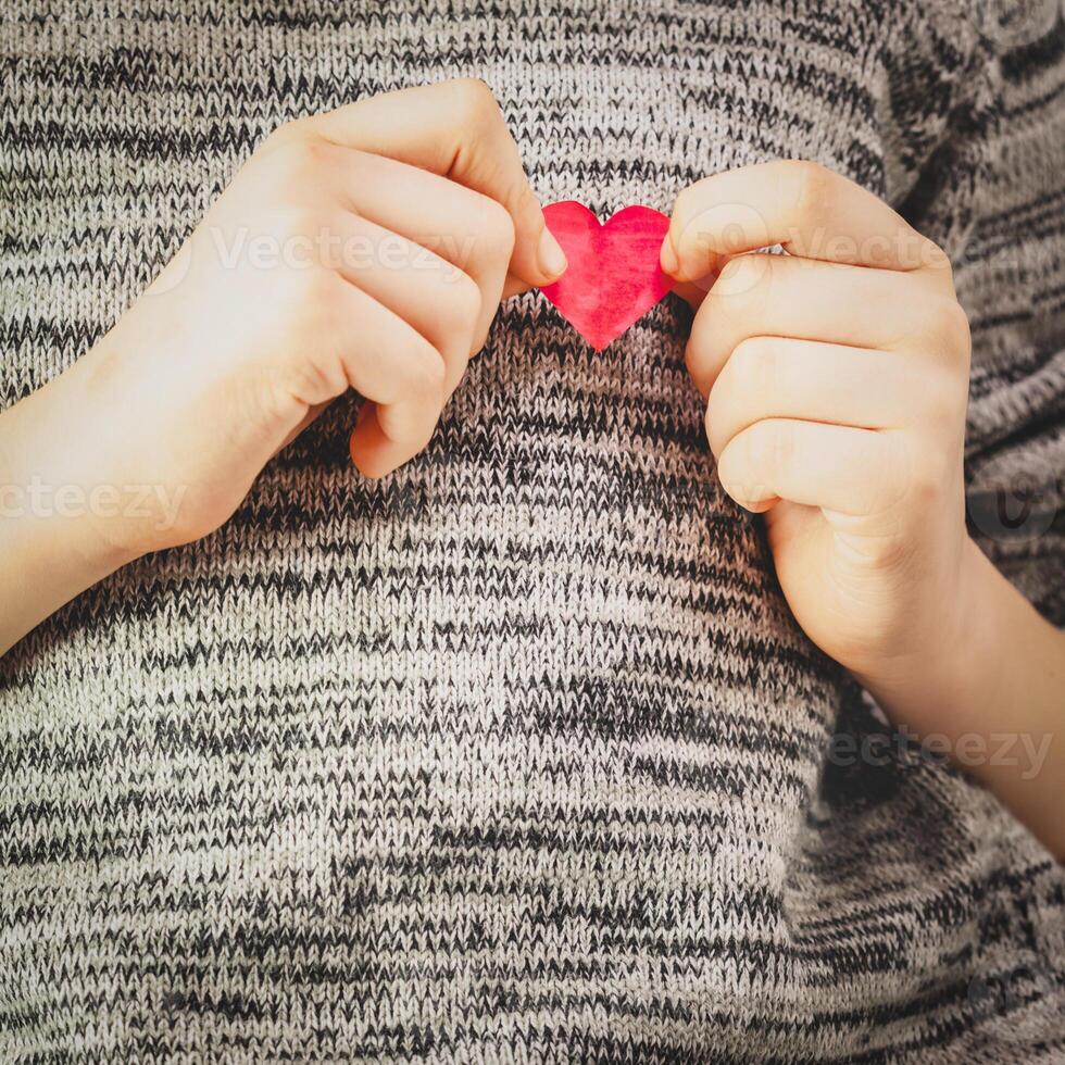 Children's hands hold a heart drawn, cut out and painted red photo