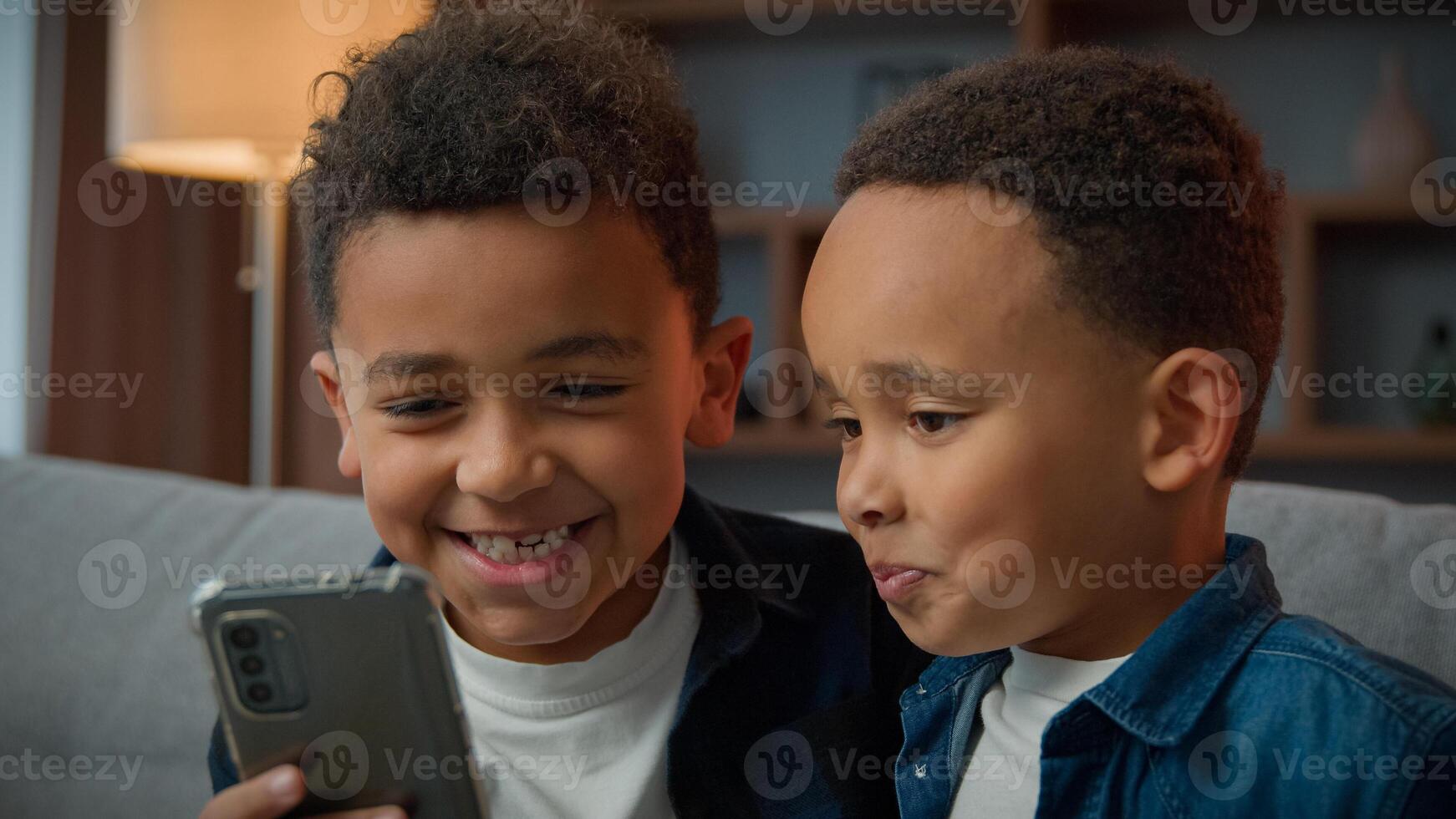 Two African American little boys brothers laughing browsing mobile phone without parents bad behavior young generation children and modern technology addicted kids siblings using funny smartphone app photo