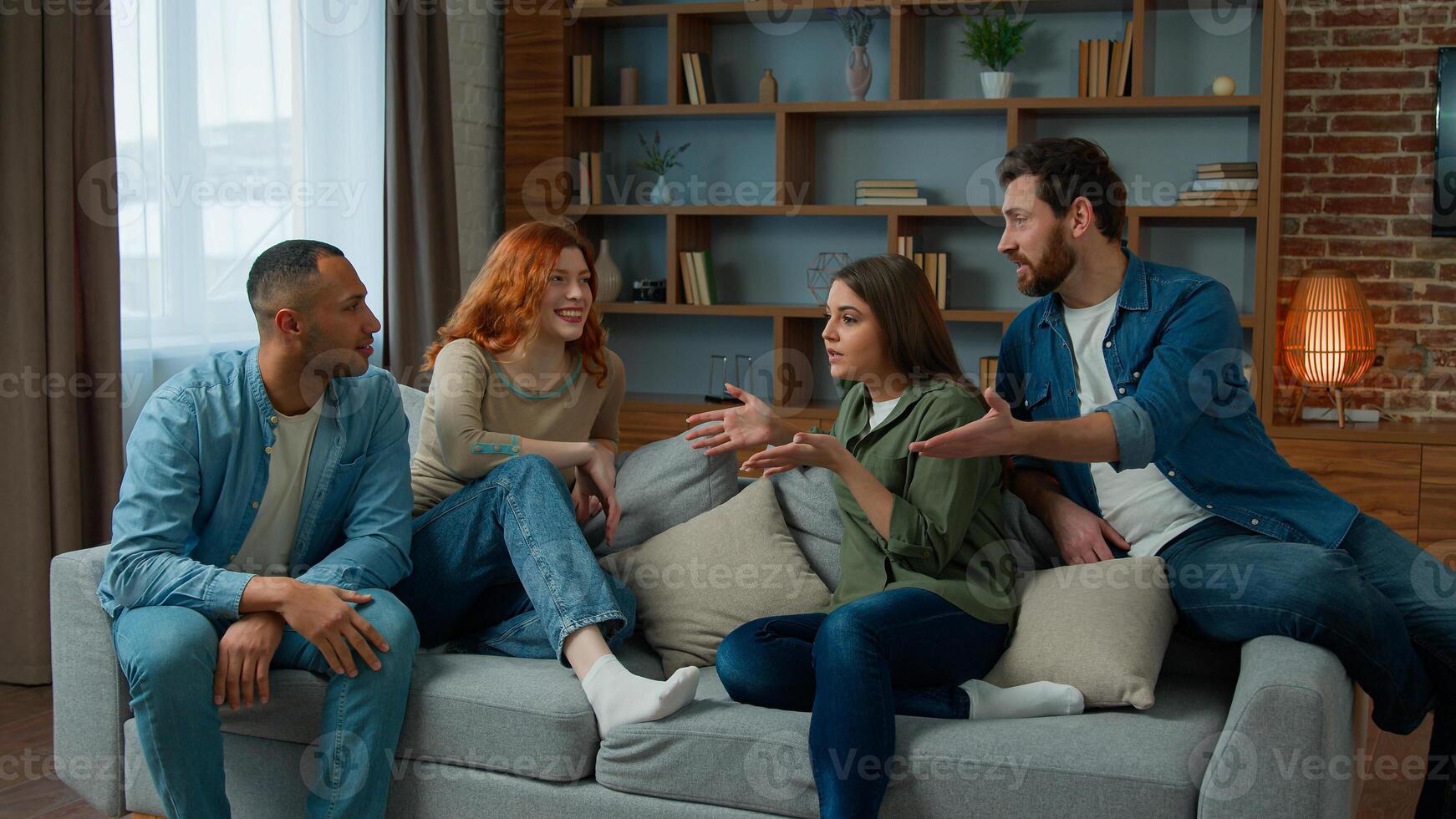 Group of diverse ethnic multiracial friends girls guys sit on sofa at home talking argue conflict friendly dispute debate discussing problem ambitious expressive men women arguing discussion indoors photo