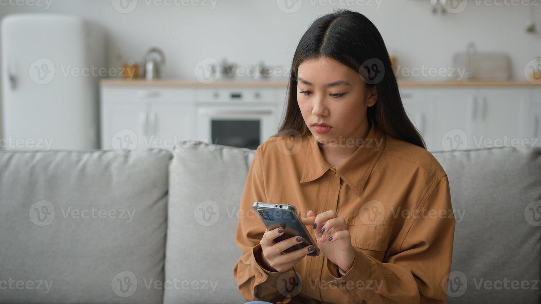 Sad disappointed upset woman Asian chinese japanese girl lady in kitchen reading bad news in chat app on mobile phone failure connection mistake trouble rejected email lost message smartphone problem photo